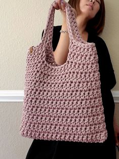 a woman holding a pink crocheted bag in front of her face while standing next to a wall