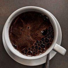 a white cup filled with liquid on top of a saucer next to a spoon