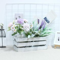 an arrangement of flowers in a wooden crate on a table with pictures and frames behind it