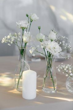 three vases filled with white flowers on top of a table next to a candle