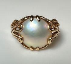 Offered is a lovely, well constructed vintage Mabe Pearl ring. The pearl has a subtle lavender/pink iridescence and it's in a nice low profile setting. Each side has butterfly design. Very pretty ring. 4.8g 14k solid yellow gold Hallmarked Mabe Pearl 12 x 12 mm S 7 US Fine vintage condition Luxury Antique Cabochon Pearl Ring, Elegant Round Opal Ring For Formal Occasions, Elegant Round Opal Ring For Formal Events, Heirloom High Luster Oval Pearl Ring, Formal Cabochon Pearl Ring, Formal 14k Gold Pearl Ring With High Luster, Formal Oval Cabochon Pearl Ring, Formal Moonstone Ring, Antique Pearl Ring With Cabochon For Formal Occasions