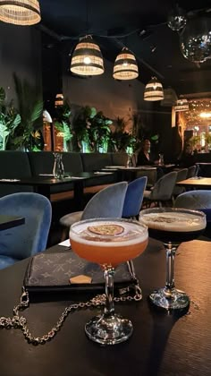 two drinks sitting on top of a table in front of some chairs and chandeliers