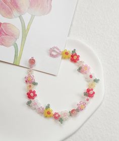 a white plate topped with pink flowers next to a greeting card and jewelry set on top of a table