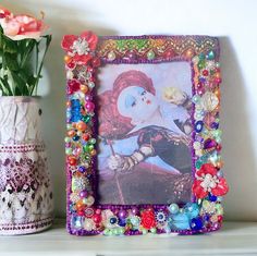 there is a picture frame with beads and flowers on the shelf next to it,