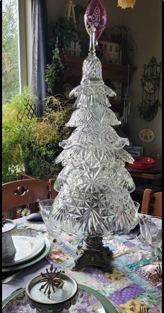 a glass christmas tree sitting on top of a table next to plates and utensils