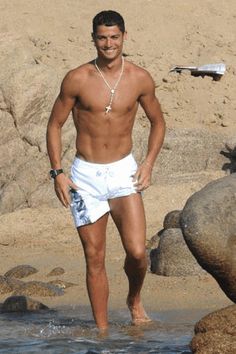 a shirtless man standing in the water near some rocks and boulders, with his hands on his hips