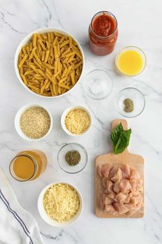 ingredients to make pasta in bowls on a white marble countertop, including meat and cheese