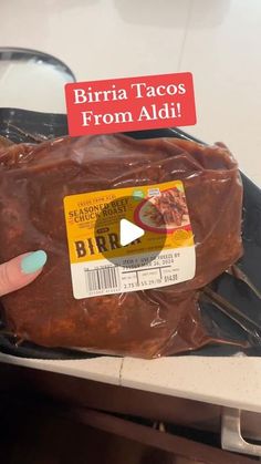 a person holding up a piece of meat in an oven with the label birra tacos from aldi