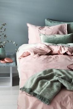 a bed with pink and green comforters in a room next to a vase filled with flowers