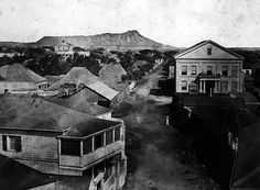 an old black and white photo of a town with mountains in the backround