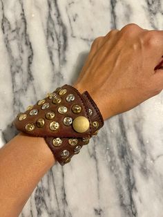 a woman's hand wearing a brown leather bracelet with gold rivets