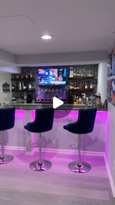 a bar with three blue stools in front of it and a television on the wall