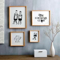 three framed pictures hang on the wall above a wooden table with a vase and plant