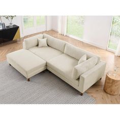 a white sectional sofa sitting on top of a rug in a living room next to a window