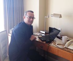 a man sitting at a desk with a laptop computer and phone on top of it