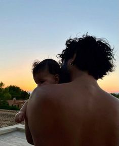 a man holding a baby in his arms at the top of a roof while the sun sets