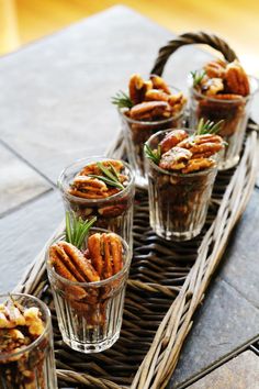 small glass cups filled with nuts sitting on top of a wicker tray next to two glasses