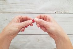 two hands are holding something red and white in front of a wooden wall with wood planks