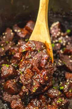 a wooden spoon is full of cooked meat and seasoning in a pot with black rice