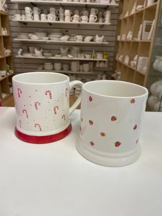 two coffee mugs sitting on top of a table next to each other in front of shelves