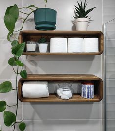 two wooden shelves holding toilet paper and other bathroom items next to a potted plant