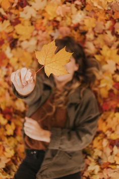 a woman holding up a yellow leaf in front of her face with autumn leaves around her