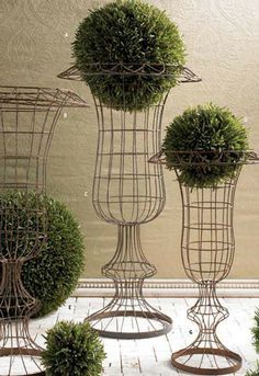 four metal vases with plants in them sitting on the floor next to each other