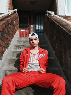 a young man sitting on the steps in front of a building wearing red sweatpants and a white hat