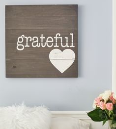 a wooden sign that says grateful with a white heart on it next to a flower vase