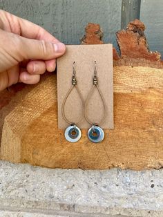 a pair of earrings is being held up by a hand on a piece of wood