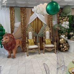 a room decorated in gold, green and white with balloons hanging from the ceiling next to a lion statue