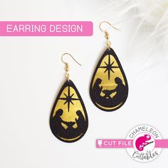 pair of earrings with gold and black designs on them, sitting next to white feathers