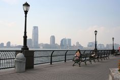 a woman sitting on a bench next to the water with a city in the background