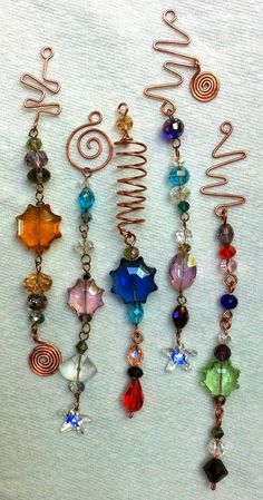 several different colored beads and charms hanging from a metal hook on a white cloth background