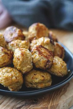 a black plate filled with meatballs on top of a wooden table