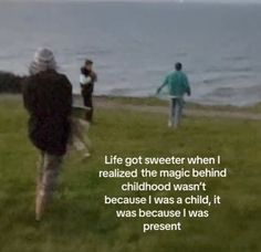 three people are walking in the grass by the water