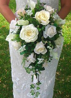 a woman in a wedding dress holding a white bouquet with green and white flowers on it