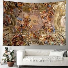 a large tapestry hanging on the wall above a couch in a room with white furniture and potted plants