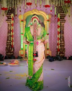 a woman in a green and pink sari is standing near a stage with flowers