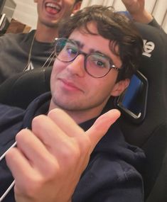 two young men sitting next to each other in front of a tv holding their thumbs up