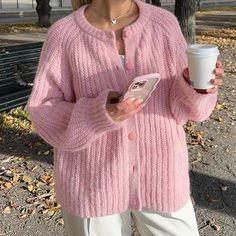 a woman in pink sweater holding a cup and cell phone