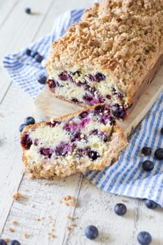 a loaf of blueberry bread sitting on top of a wooden cutting board next to fresh blueberries