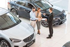 two men and a woman standing in front of three parked cars, talking to each other