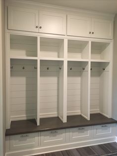 an empty white mud room with built - in cabinets and drawers on the wall, along with wood flooring