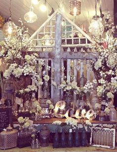 a table topped with lots of vases filled with white flowers and greenery next to a wooden fence