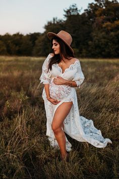 a pregnant woman in a white dress and hat poses for a photo while standing in tall grass