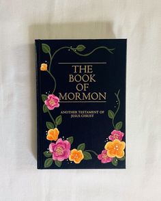 the book of mormon is laying on top of a white sheet with flowers painted on it