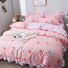 a bed with pink sheets and strawberry print on the comforter, along with two pillows