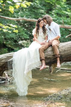 a man and woman are sitting on a tree branch in the middle of a stream