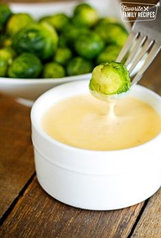 a spoon full of broccoli being held over a bowl filled with cheese sauce